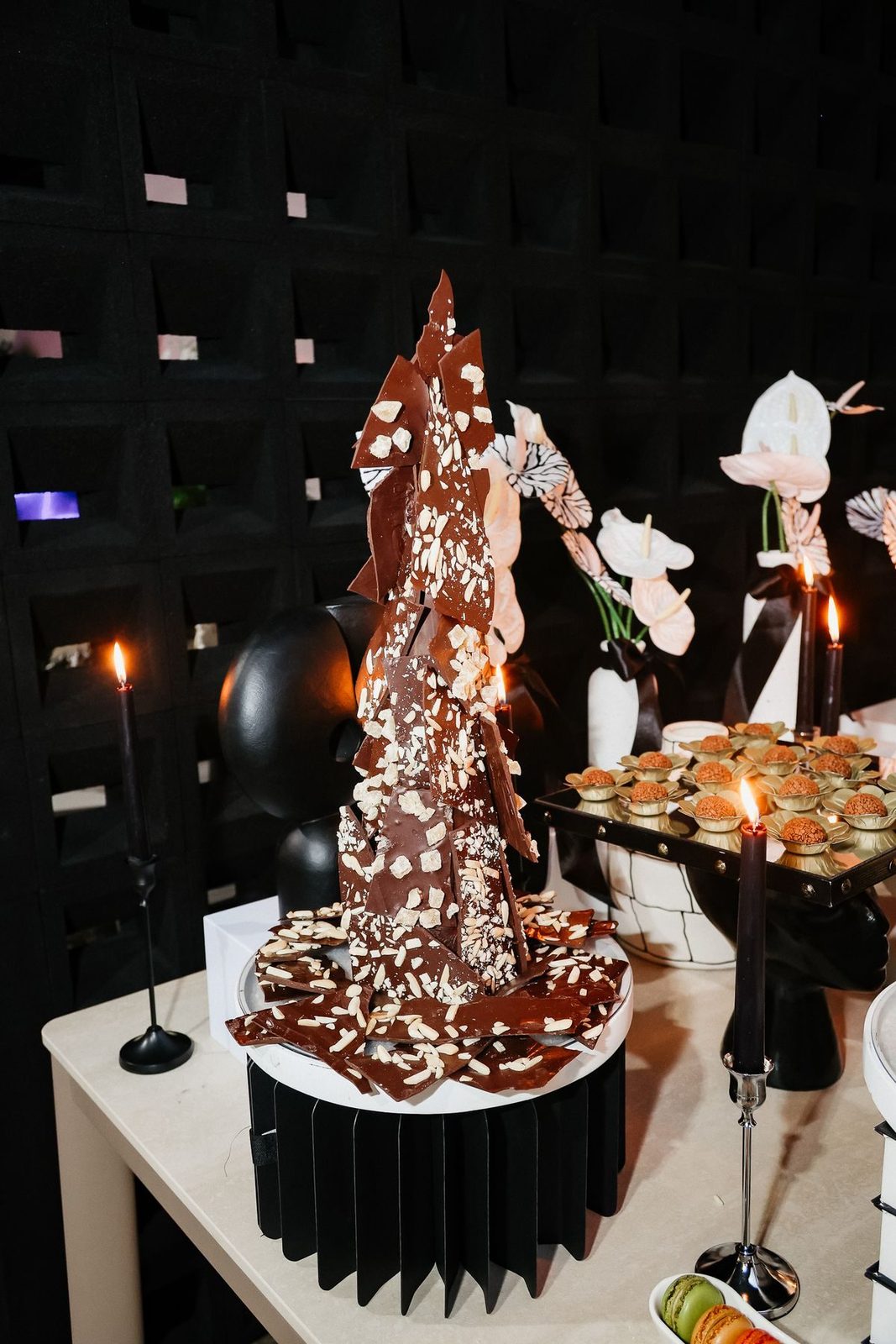 Tower of chocolate bark beside candles and truffles